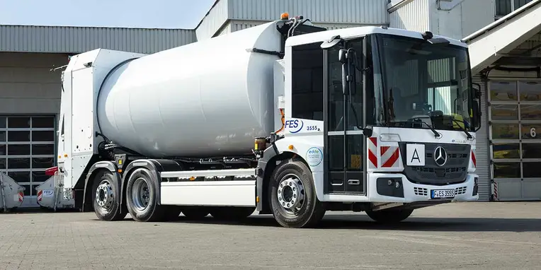 Ein Mercedes-Benz Betonmischer mit einem großen, weißen Zementtank steht auf einem asphaltieren Gelände, bereit zum Einsatz.