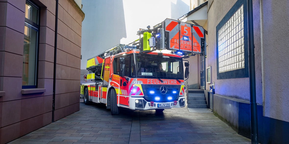Feuerwehrfahrzeug fährt durch eine enge Gasse mit eingeschaltetem Blaulicht.