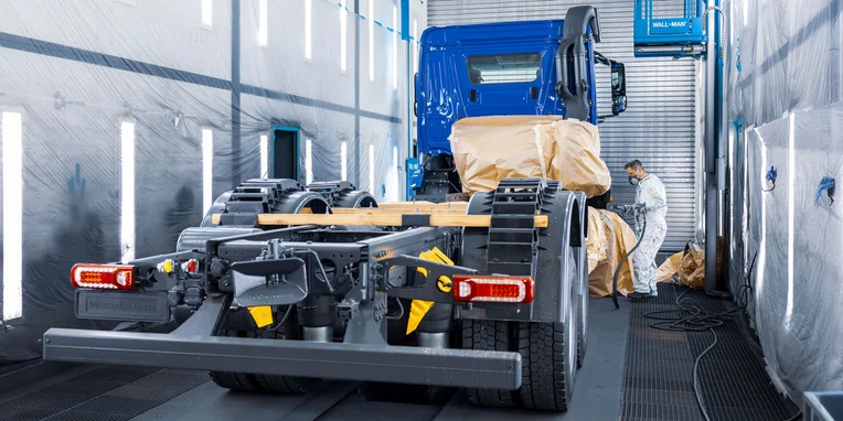 Camion Mercedes-Benz in fase di preparazione per la verniciatura, con operatore che lavora in un ambiente industriale ben illuminato.