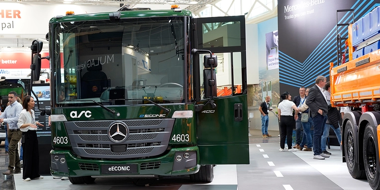 Mercedes-Benz eCONIC-Lkw steht mit geöffneter Tür auf einer Messe, umgeben von Interessierten, die verschiedene Modelle und technische Details betrachten.