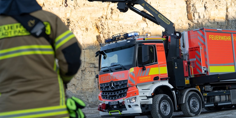 Feuerwehrmann mit Schutzkleidung steht vor einem Feuerwehr-Actros mit Kranaufbau.