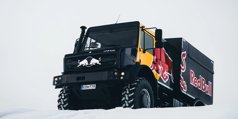 Ein roter und schwarzer Truck mit dem Red Bull-Logo steht auf schneebedecktem Boden, bereit für einen Transport in winterlichen Bedingungen.