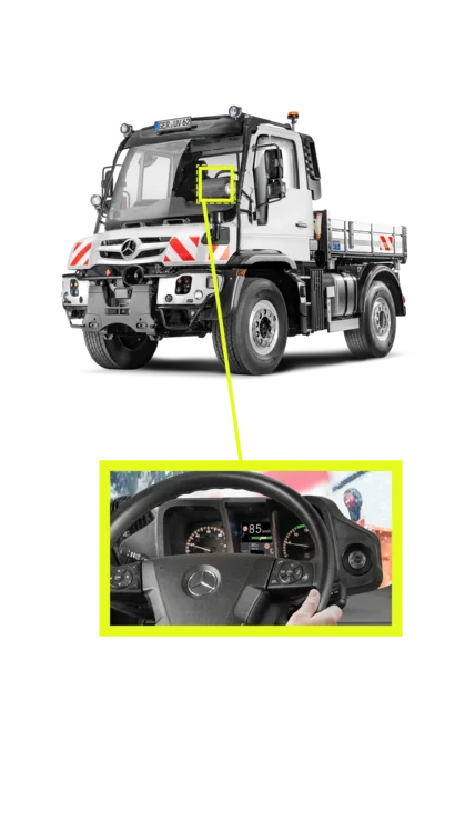 Der Unimog von Mercedes-Benz wird frontal dargestellt, während das Bild eine Zoomansicht des Armaturenbretts zeigt, mit einem Überblick über das Lenkrad und Displays.