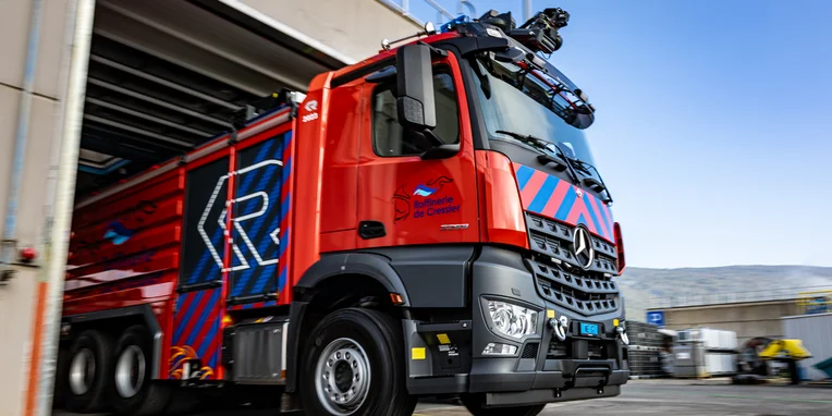 Ein roter Mercedes-Benz Lkw fährt aus einem Lagerhaus. Das Fahrzeug ist mit auffälligen blauen und roten Mustern verziert und zeigt an der Seite das Logo der Firma.