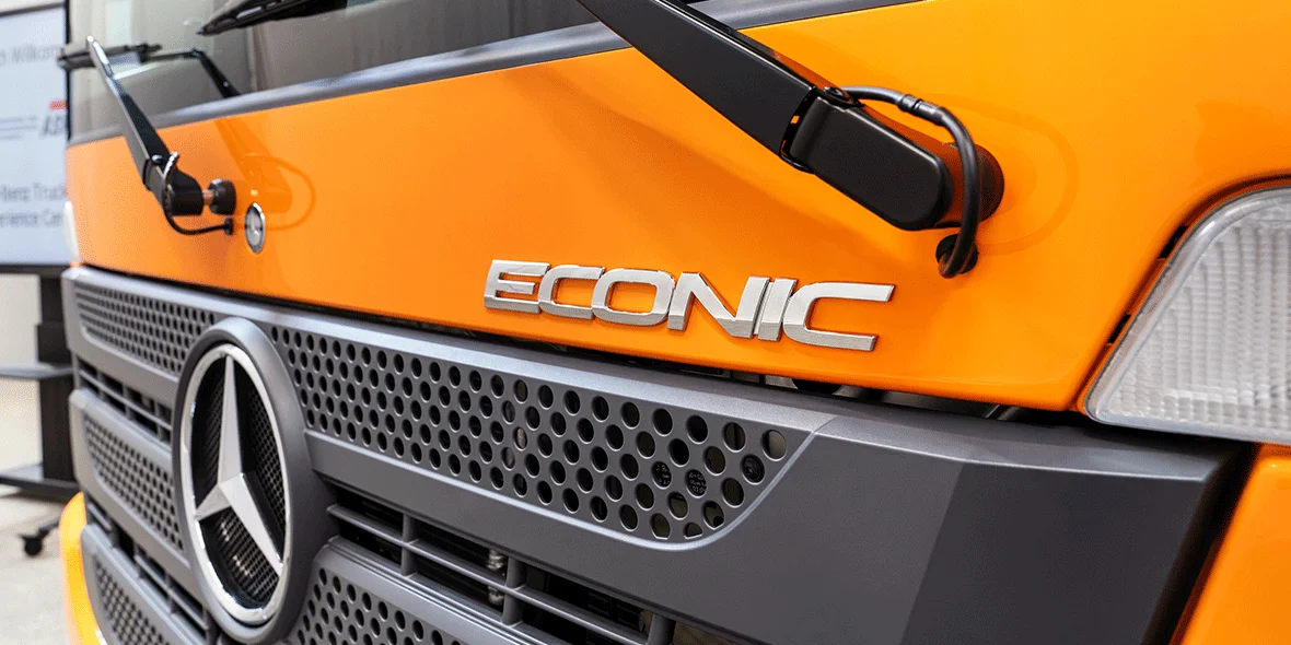 Vorderansicht eines Mercedes-Benz Econic Fahrzeugs in leuchtendem Orange, mit dem markanten Stern-Logo und den Wischern prominent dargestellt.