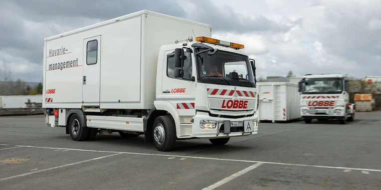 Ein Mercedes-Benz Lkw mit einem großen weißen Kastenaufbau, der "LOBBE" und "Havarie-Management" beschriftet ist, fährt auf einem Parkplatz.