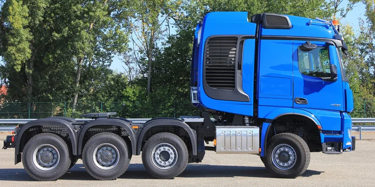Camion Mercedes-Benz di colore blu, visto di lato, con cabina alta e tre assi posteriori, parcheggiato su una superficie asfaltata.