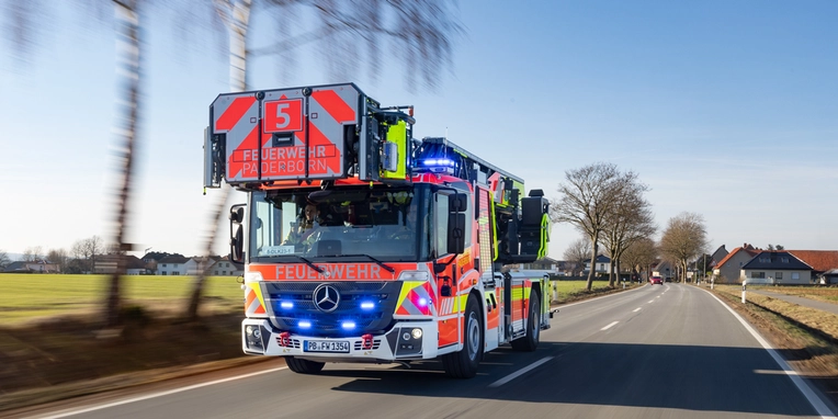 Feuerwehrfahrzeug fährt mit eingeschaltetem Blaulicht auf einer Landstraße.