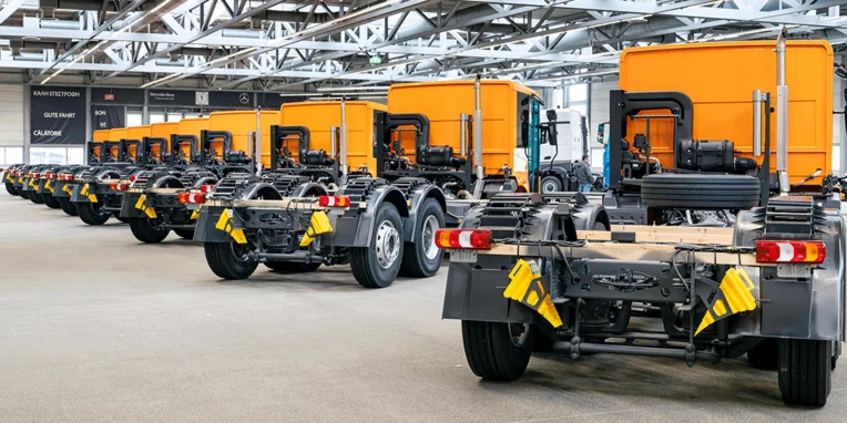 Reihe von Fahrgestellen mit gelben Aufbauten, die in einer modernen Fabrikhalle von Mercedes-Benz ausgestellt sind, bereit für die Montage oder den Versand.