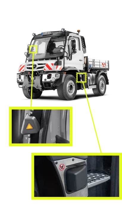 Ein Mercedes-Benz Unimog, ausgestattet mit einem Ladebett, zeigt Markierungen für Sicherheitsfunktionen. Nahaufnahmen zeigen einen Blinklichtschalter und einen Fußschalter im Fahrerbereich.
