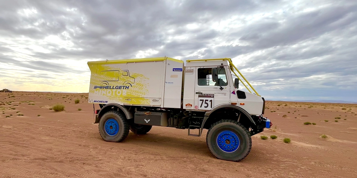 Ein geländegängiger Mercedes-Benz Lkw steht in einer sandigen Wüstenlandschaft. Das Fahrzeug hat eine helle, gelbe Lackierung mit der Nummer 751 und ist bereit für ein Abenteuer.